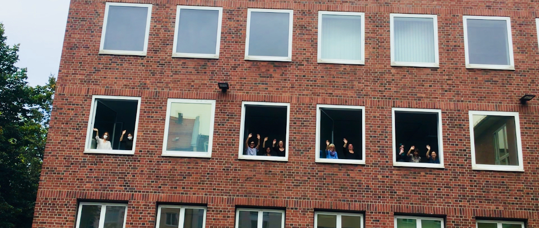 Menschen winken fröhlich aus den Fenstern eines Bürogebäudes